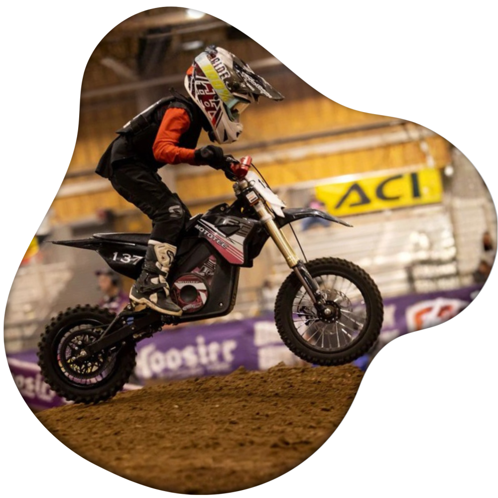 Child riding a motocross bike indoors on a dirt track.
